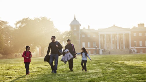 A family walking in the grounds at Osterley Park and House, London, the house is in the background and there are rays of sun coming onto the grass